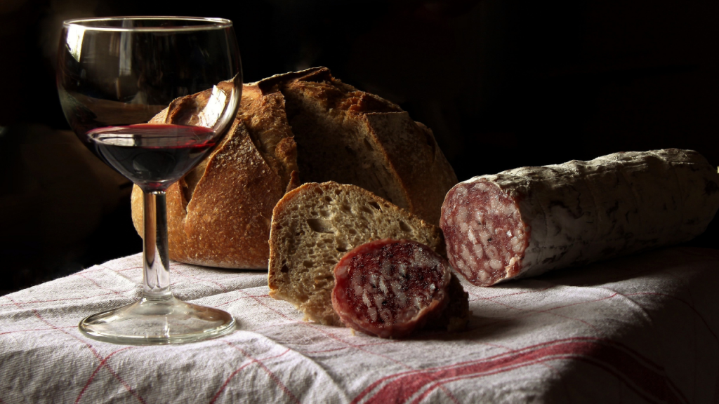 Calice di vino rosso dei Colli Orientali su tavolo in legno insieme a pane fatto in casa e salame nostrano, uno dei possibili abbinamenti de Le Grandi Verticali delle Città del Vino 2026.